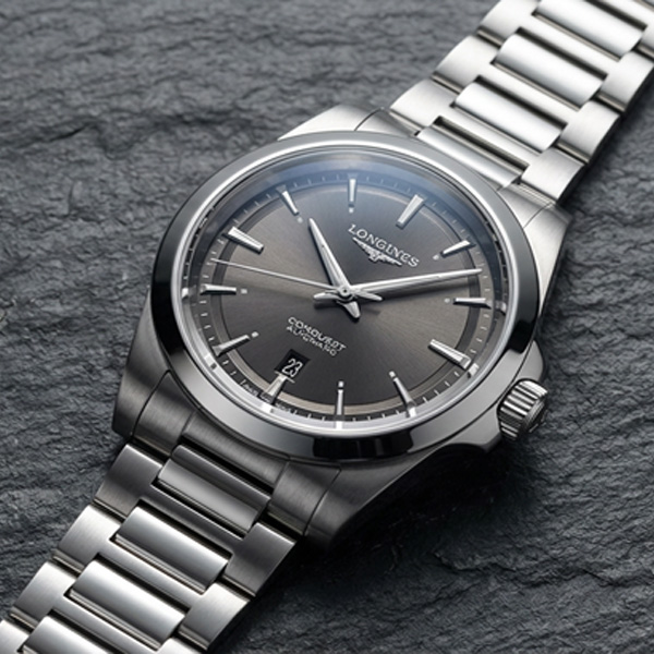 Longines Conquest Automatic with grey sunray dial and polished steel bracelet resting on natural slate stone, Swiss automatic everyday watch