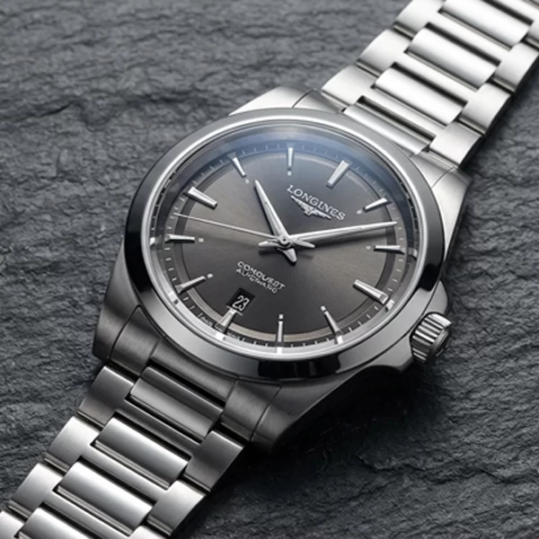 Longines Conquest Automatic with grey sunray dial and polished steel bracelet resting on natural slate stone, Swiss automatic everyday watch