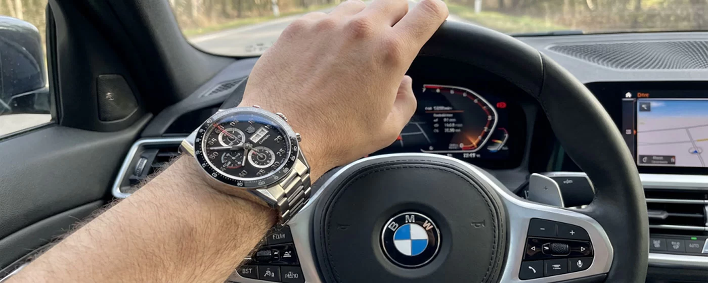 TAG Heuer Carrera Chronograph on a wrist resting on a car steering wheel shot from the driver's perspective with blurred dashboard in the background