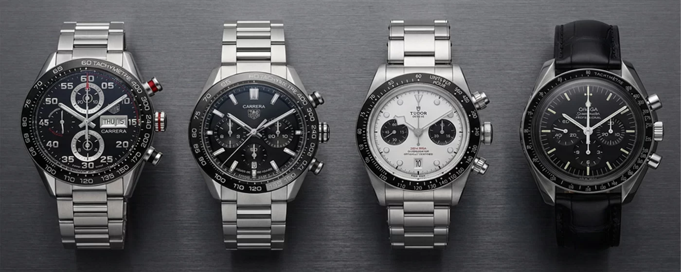 Four watches arranged side by side from left to right TAG Heuer Carrera Calibre 16 TAG Heuer Carrera Heuer 02 Tudor Black Bay Chrono and Omega Speedmaster Professional Moonwatch photographed from directly above on dark slate