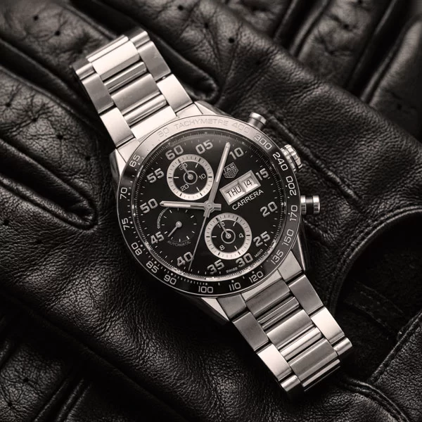 Vintage 1963 TAG Heuer Carrera chronograph with silver dial and black sub-dials photographed flat on dark leather in black and white