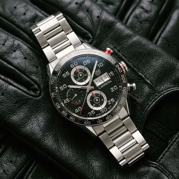Modern TAG Heuer Carrera Chronograph with black dial and steel bracelet photographed flat from above on dark leather surface