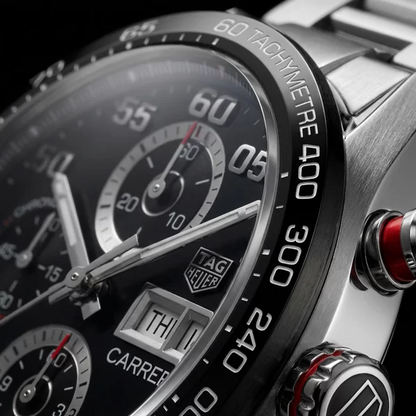 Close-up macro of TAG Heuer Carrera black ceramic tachymeter bezel showing white tachymeter scale numerals and polished steel case edge