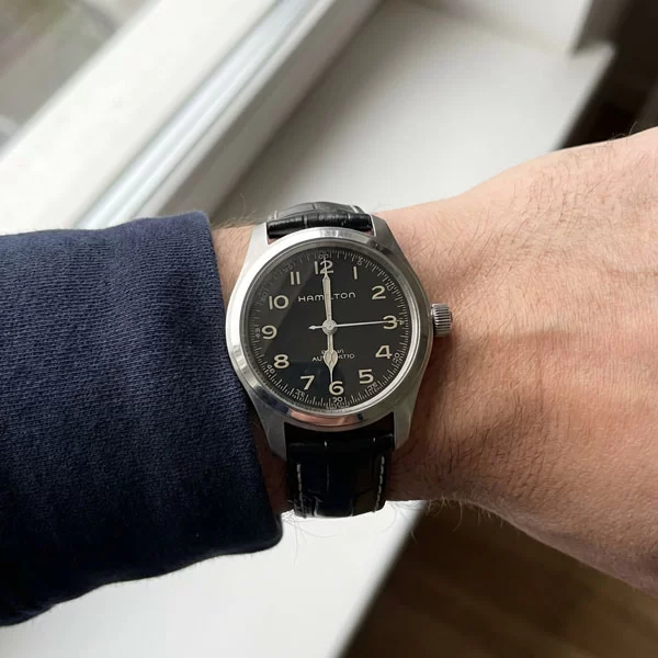 Hamilton Khaki Field Murph 38mm watch with black dial and black leather strap worn on a wrist with a dark navy casual sleeve, photographed from the side near a window in natural light
