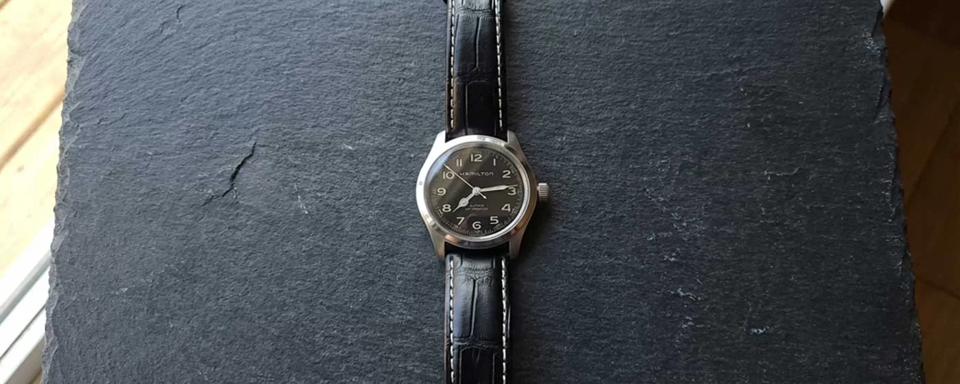 Hamilton Khaki Field Murph 38mm watch with black dial and black crocodile-embossed leather strap with white contrast stitching laid flat on a dark slate stone surface, photographed from directly above in natural light