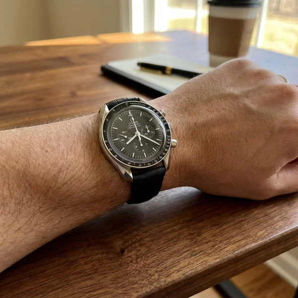 Omega Speedmaster Professional Moonwatch with black alligator leather strap worn on the wrist resting on a wooden table