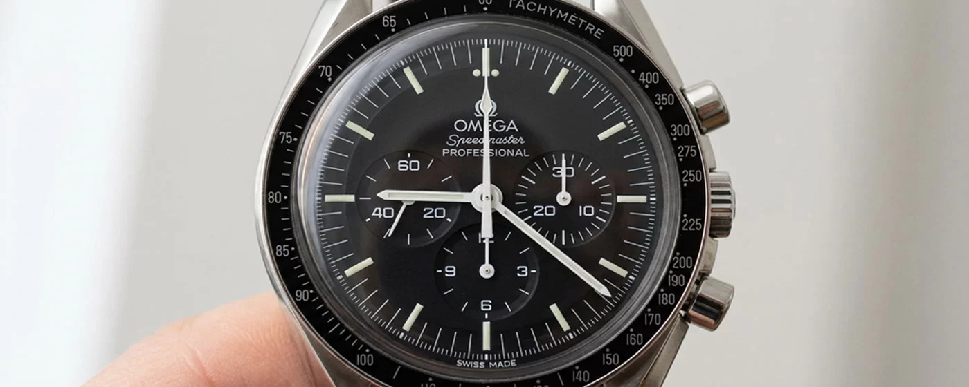 Close-up of the Omega Speedmaster Professional Moonwatch matte black dial showing the tri-compax sub-registers, tachymeter bezel, and white baton hands
