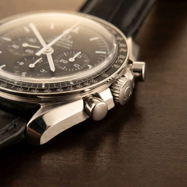 Close-up of the Omega Speedmaster Professional Moonwatch case side showing the chronograph pushers, winding crown, and brushed steel finishing on a dark surface